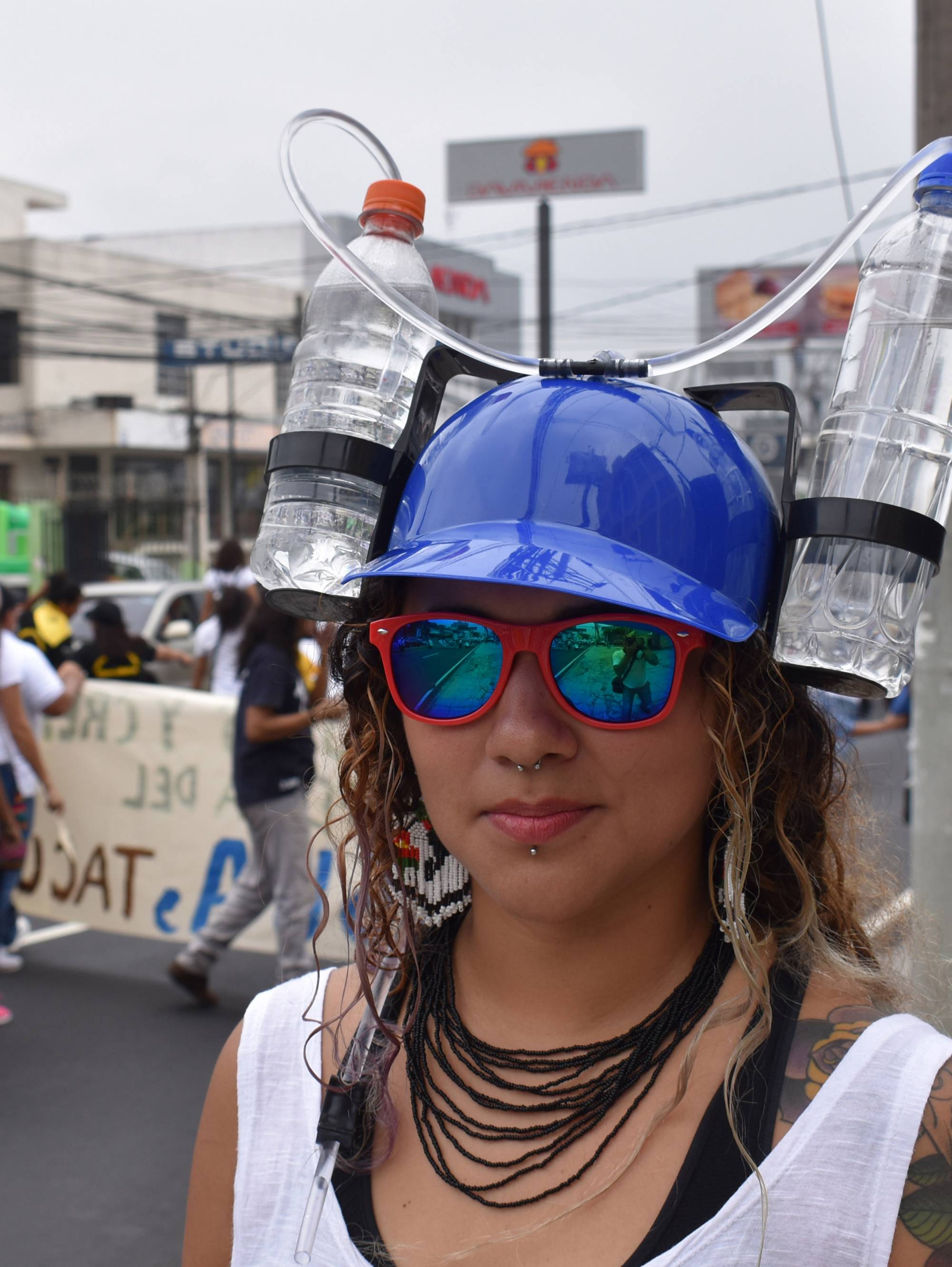 Young woman in sunglasses wearing hat with water bottle attached to either side with drinking tube